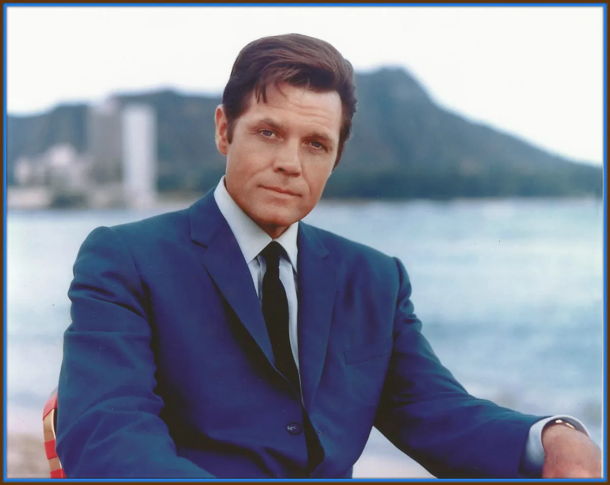 A man in a dark suit seated outdoors in Hawai'i with Diamond Head in the background